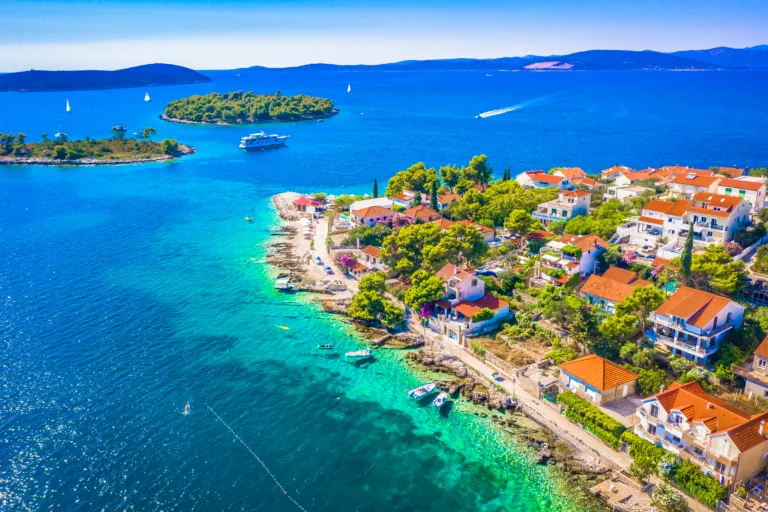 A beautiful aerial view of the Mediterranean landscape surrounding Maslinica on Solta Island, Croatia, featuring pine forests, traditional stone houses, and the deep blue Adriatic Sea