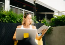 Kako postaviti rutino, ki bo dejansko zdržala več kot en teden? A relaxed digital nomad woman in sportswear sits on an outdoor resort couch, writing and planning in her notebook during a peaceful wellness morning.