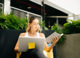 Kako postaviti rutino, ki bo dejansko zdržala več kot en teden? A relaxed digital nomad woman in sportswear sits on an outdoor resort couch, writing and planning in her notebook during a peaceful wellness morning.