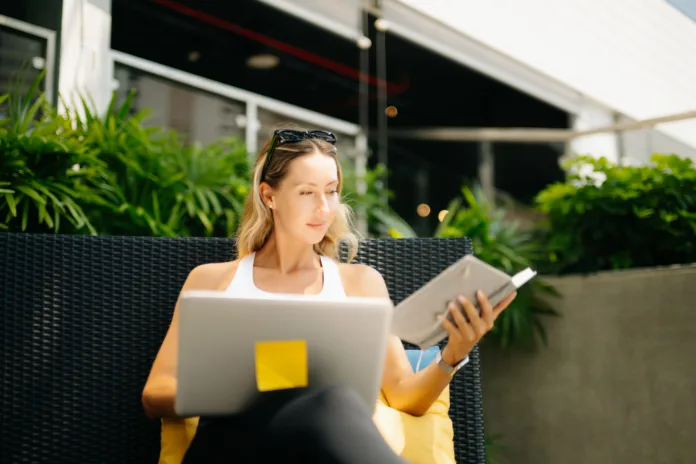 a-relaxed-digital-nomad-woman-in-sportswear-sits-on-an-outdoor-resort-couch-writing-and-planning-in-her-notebook-during-a-peaceful-wellness-morning-stockpack-istock A relaxed digital nomad woman in sportswear sits on an outdoor resort couch, writing and planning in her notebook during a peaceful wellness morning.