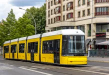 Se v Ljubljano vrača tramvaj? Novica je občane pustila ravnodušne A yellow city tram moves past a rounded facade with motion blur, conveying speed, comfort, and sustainable urban mobility.
