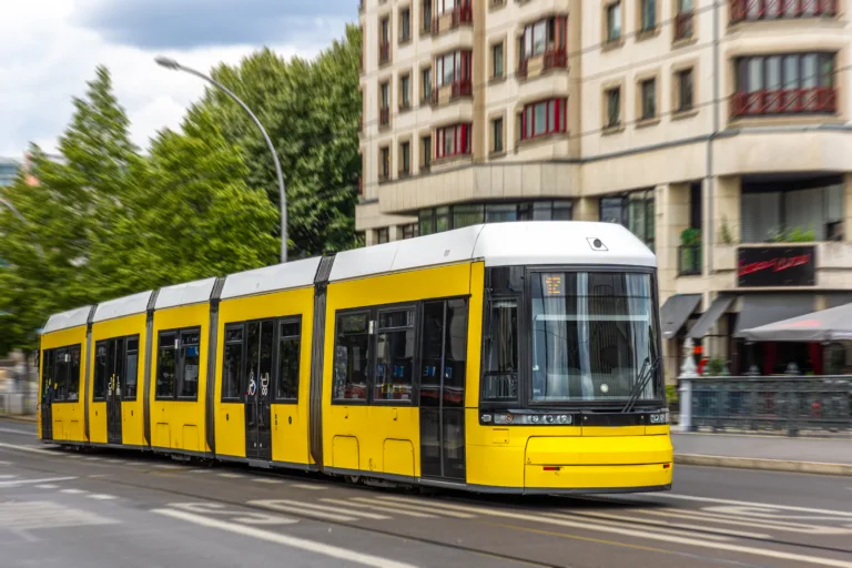 A yellow city tram moves past a rounded facade with motion blur, conveying speed, comfort, and sustainable urban mobility.
