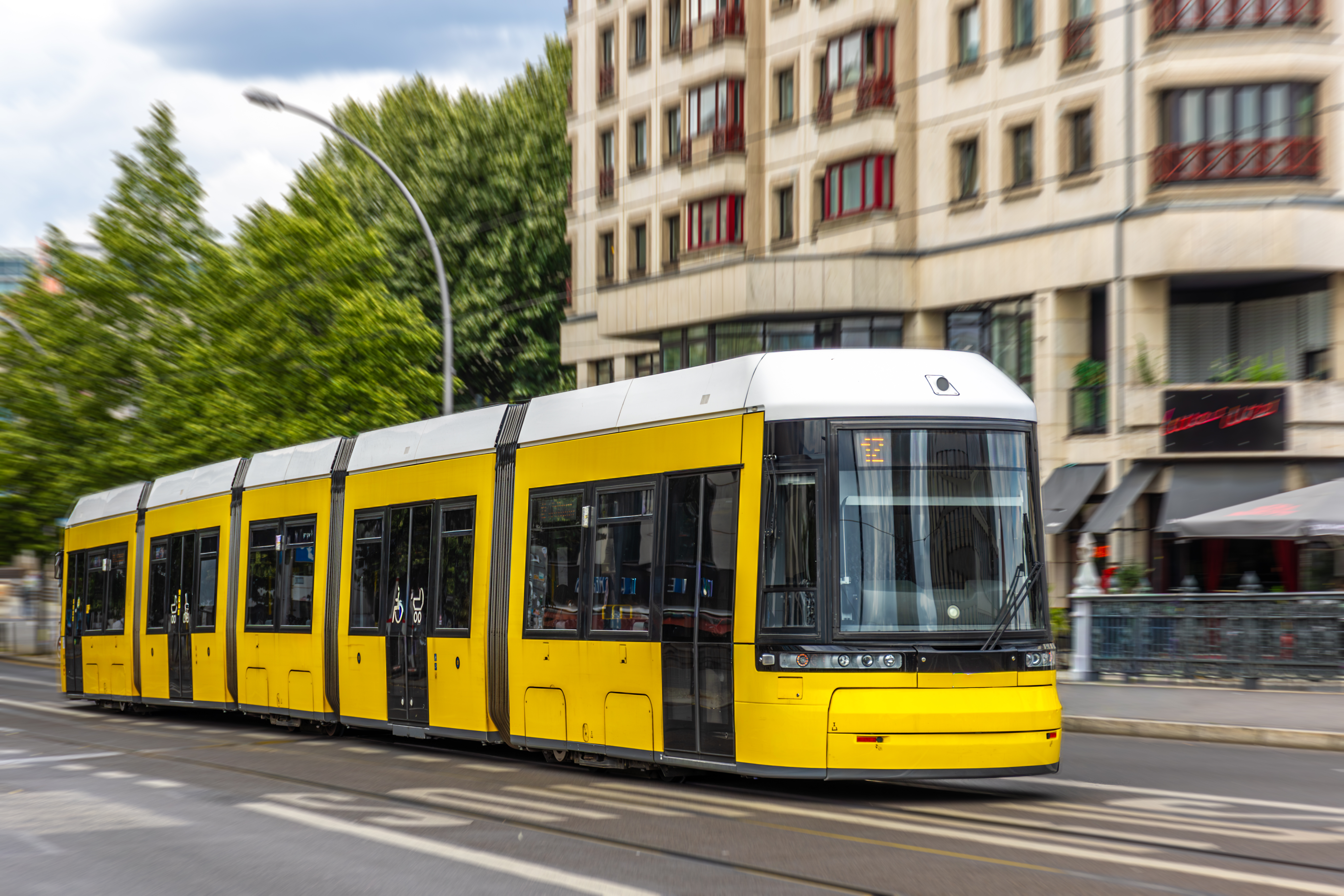 a-yellow-city-tram-moves-past-a-rounded-facade-with-motion-blur-conveying-speed-comfort-and-sustainable-urban-mobility-stockpack-istock A yellow city tram moves past a rounded facade with motion blur, conveying speed, comfort, and sustainable urban mobility.