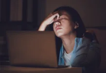Kako preživeti izpitno obdobje brez neprespanih noči in hektolitrov kave? Asian woman student or businesswoman work late at night. Concentrated and feel sleepy at the desk in dark room with laptop or notebook.Concept of people workhard and burnout syndrome.