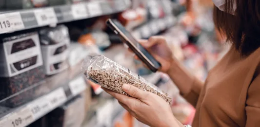 Closeup - Woman shopping in supermarket and reading product information. Costumer buying food at the market.