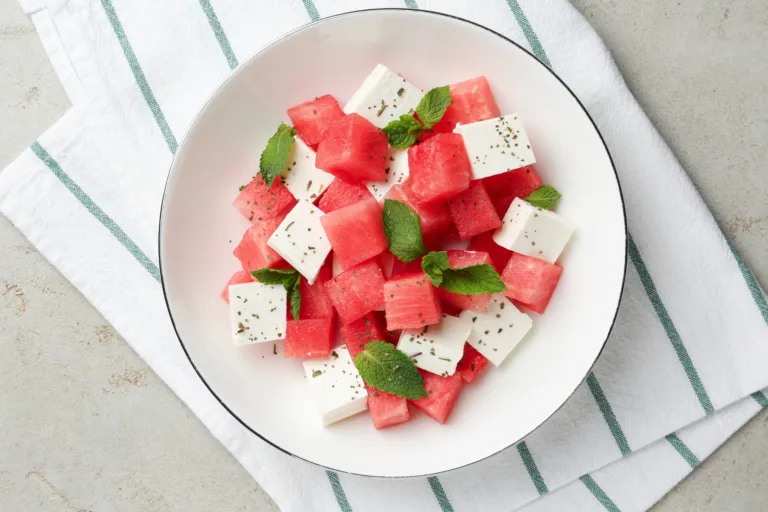 Delicious watermelon salad with mint and feta cheese in bowl on grey textured table, top view