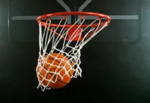 Prihodnost evropske košarke v Stožicah: Kdaj igrajo mladi slovenski upi? Detail of basketball ball hitting the hoop, top view. Isolated on black background. Freeze motion of sport action.