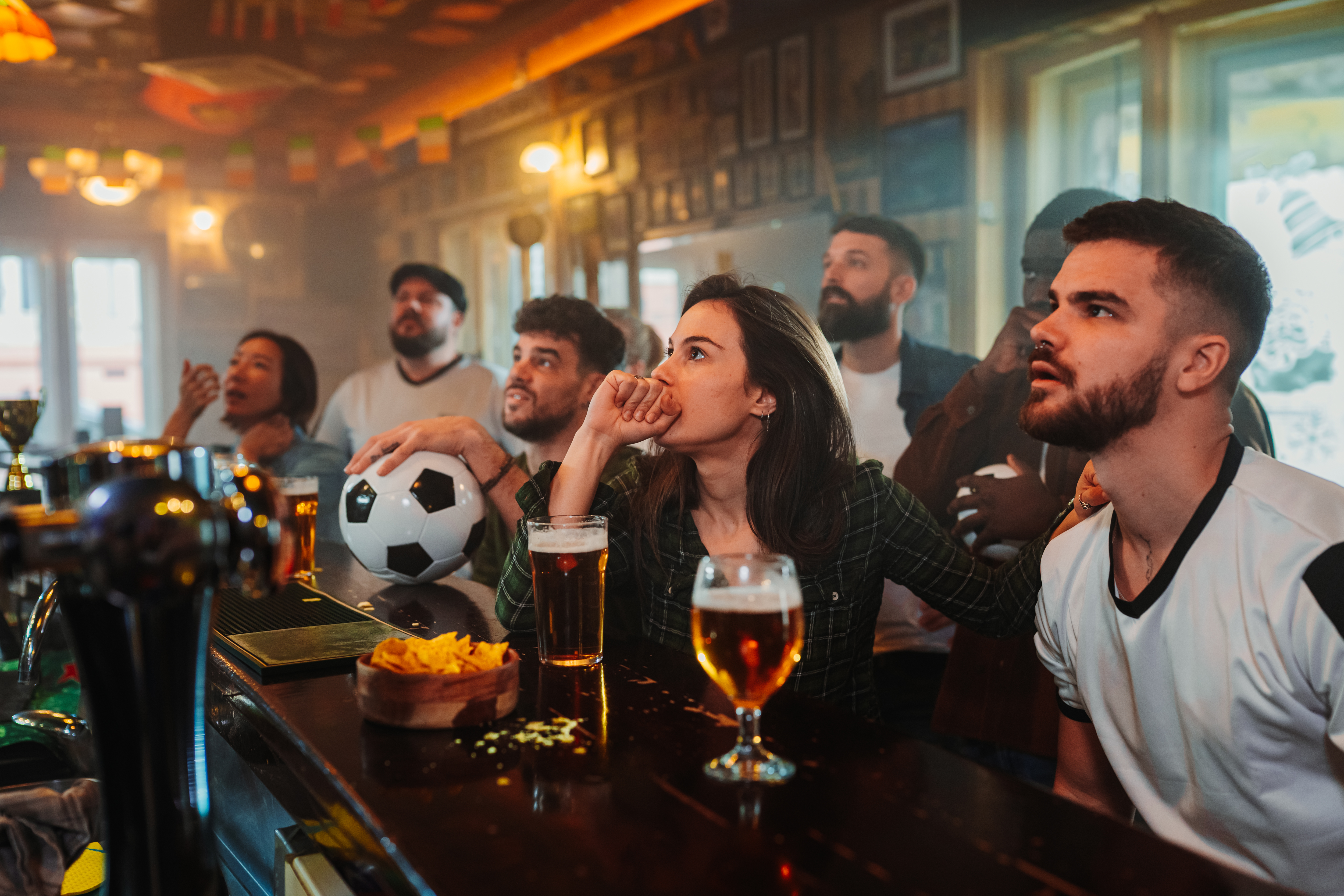 Diverse soccer fans watching a crucial game at a bar, intensely gripped by the action, sharing moments of tension and anticipation