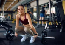 S temi štirimi vajami boste okrepili svoje kosti Happy female athlete exercising with barbell in a gym and looking at camera.