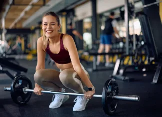 S temi štirimi vajami boste okrepili svoje kosti Happy female athlete exercising with barbell in a gym and looking at camera.