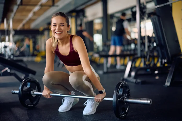 happy-female-athlete-exercising-with-barbell-in-a-gym-and-looking-at-camera-stockpack-istock Happy female athlete exercising with barbell in a gym and looking at camera.