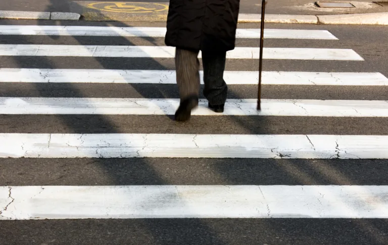 Legs and shadow of a senior person using walking cane while crossing the street in motion blur