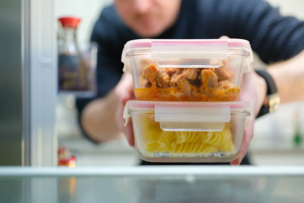 Man taking cooked pasta and chicken leftovers from the refrigerator