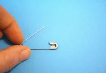 Videli ste jo že neštetokrat, a le redki vedo, čemu služi: zato ima vsaka varnostna zaponka to luknjico One metal safety pin positioned on a light blue background with hand and Copy Space, suitable for minimal concepts.