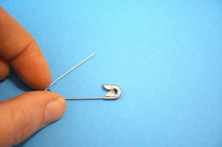 One metal safety pin positioned on a light blue background with hand and Copy Space, suitable for minimal concepts.