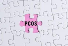Sindrom policističnih jajčnikov (PCOS) uradno preimenovan v PMOS: Zakaj je to pomembno? PCOS text on white jigsaw puzzle over pink background. Polycystic Ovary Syndrome Health Care concept.