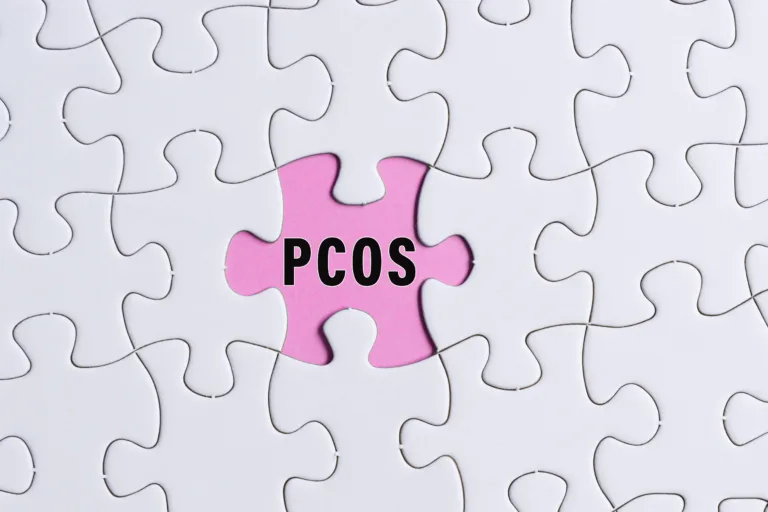 PCOS text on white jigsaw puzzle over pink background. Polycystic Ovary Syndrome Health Care concept.