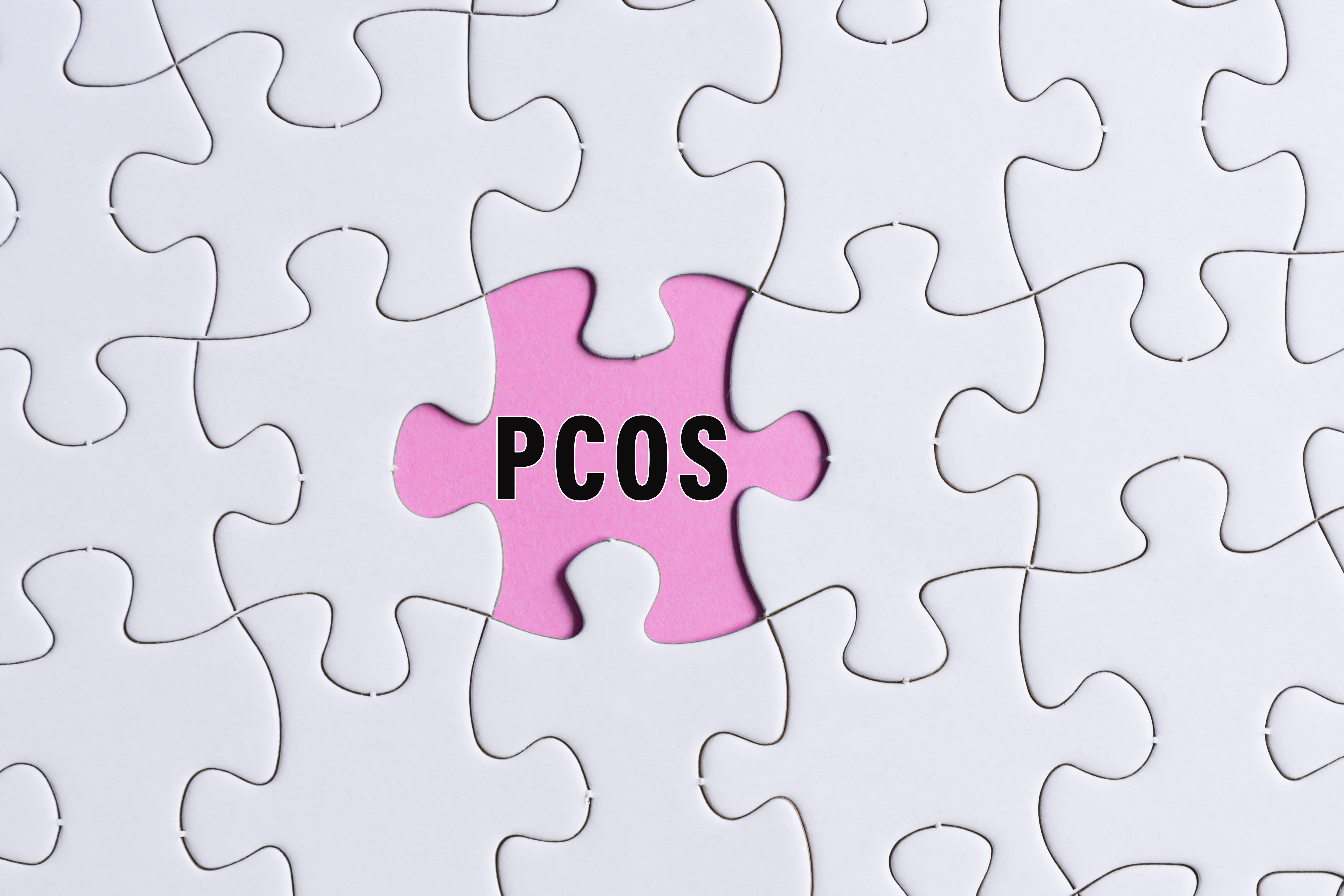 Sindrom policističnih jajčnikov (PCOS) uradno preimenovan v PMOS: Zakaj je to pomembno? PCOS text on white jigsaw puzzle over pink background. Polycystic Ovary Syndrome Health Care concept.