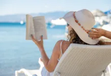 4 ljubezenski romani, ki so kot nalašč za branje na plaži Portrait of a young woman with straw hat, relaxing on the beach, reading a book