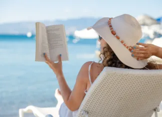 4 ljubezenski romani, ki so kot nalašč za branje na plaži Portrait of a young woman with straw hat, relaxing on the beach, reading a book