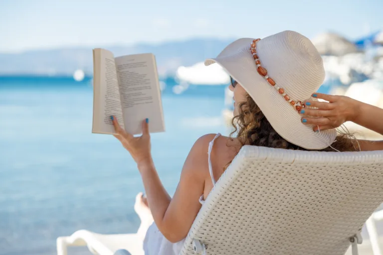 Portrait of a young woman with straw hat, relaxing on the beach, reading a book
