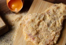 Gre meso najprej v moko ali jajca? Le eno zaporedje zagotavlja popolnoma hrustljave in sočne zrezke Raw Wiener Schnitzel, breaded steak, egg on wooden background