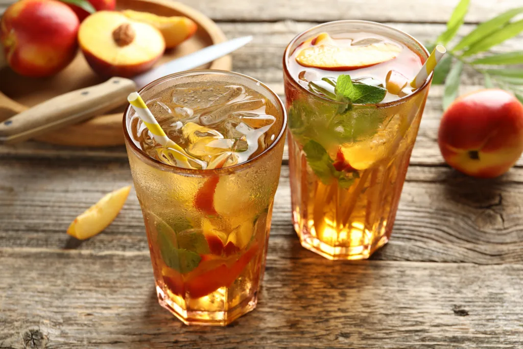 Refreshing iced peach tea in glasses and fresh fruits on wooden table, closeup