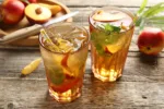 Refreshing iced peach tea in glasses and fresh fruits on wooden table, closeup