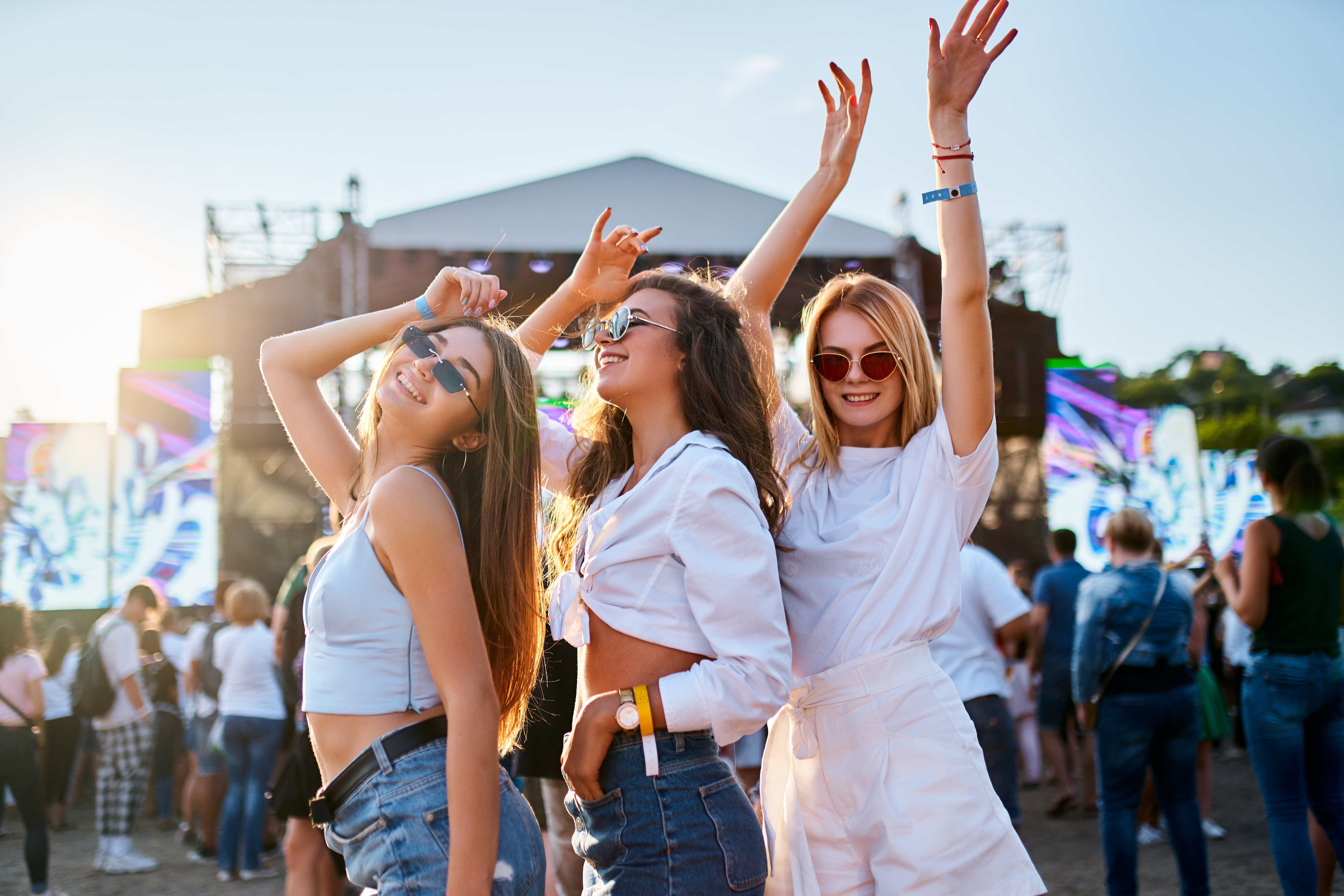 To je 5 evropskih festivalov, ki jih morate obiskati vsaj enkrat v življenju Sunlight illuminates the happy crowd, friends celebrate, party atmosphere by the ocean. Group of young women enjoying at a beach music festival, dancing together in summer outfits with sunglasses.