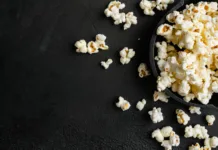 Imajo zelo malo kalorij: seznam prigrizkov, ki jih lahko jeste v neomejenih količinah Tasty salted popcorn, on black dark stone table background, top view flat lay, with copy space for text