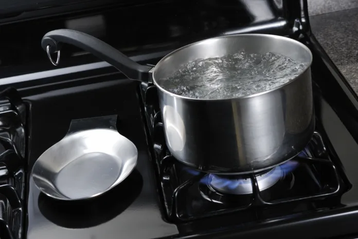Water boiling in a stainless steal pot on a black stove.