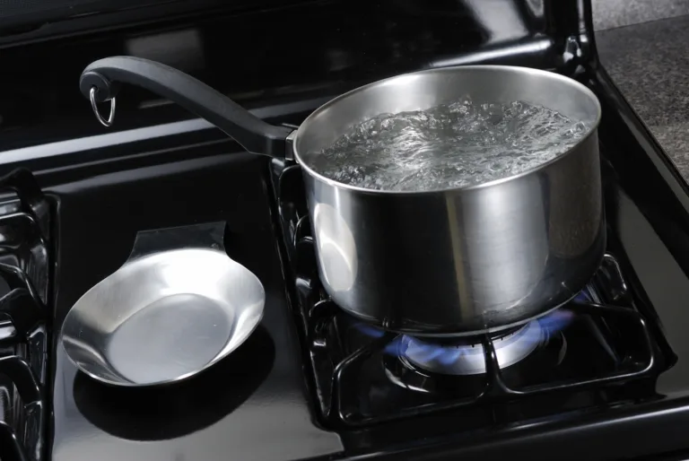 Water boiling in a stainless steal pot on a black stove.