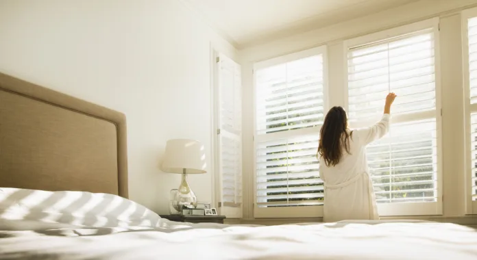 Woman in bathrobe opening bedroom window blinds