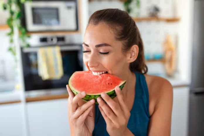 Young woman eats a slice of watermelon in the kitchen. Portrait of young woman enjoying a watermelon.
