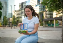 Meal Prep za cel teden: manj stroškov, manj stresa in boljša prehrana Young woman opening lunch box with a healthy fresh salad, enjoying a break in the city