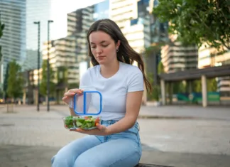 Meal Prep za cel teden: manj stroškov, manj stresa in boljša prehrana Young woman opening lunch box with a healthy fresh salad, enjoying a break in the city