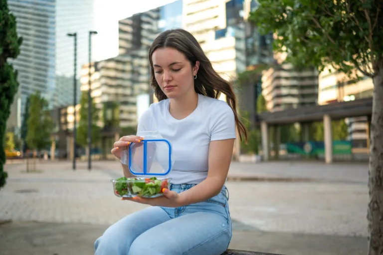 Young woman opening lunch box with a healthy fresh salad, enjoying a break in the city