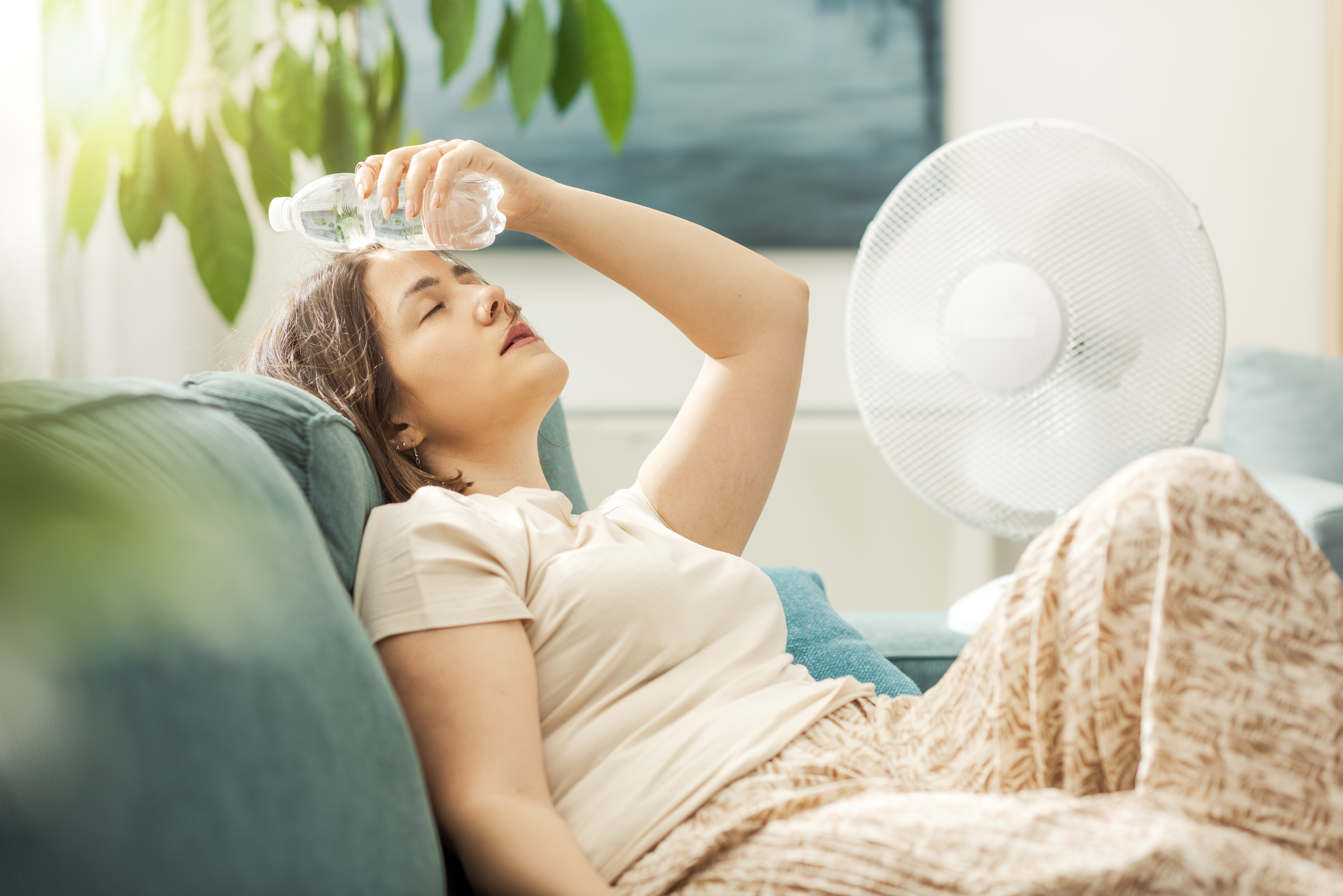 To so najboljši skriti kotički Ljubljane za pobeg pred poletno vročino Young woman sitting on the couch at home and keeping a fresh water bottle on her forehead, she is suffering from the heat