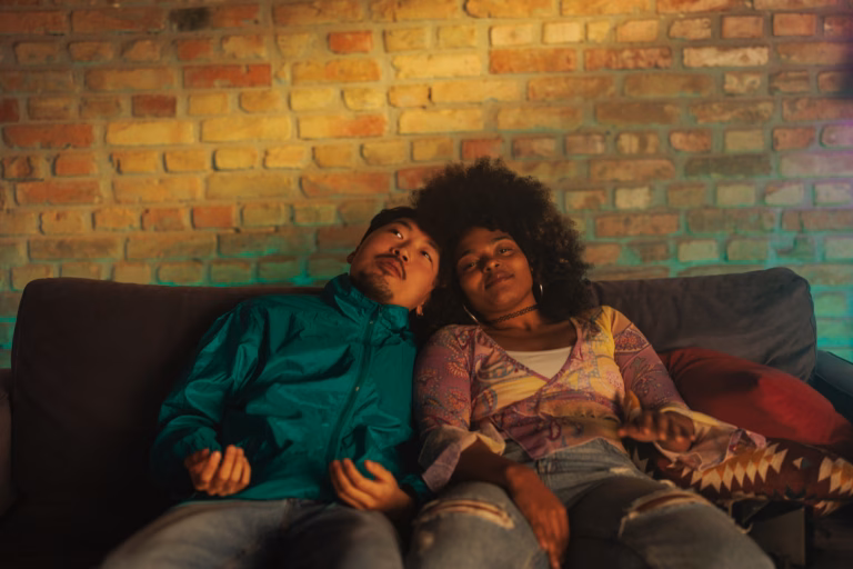 A stylish multiethnic couple is relaxing on a sofa at home.
