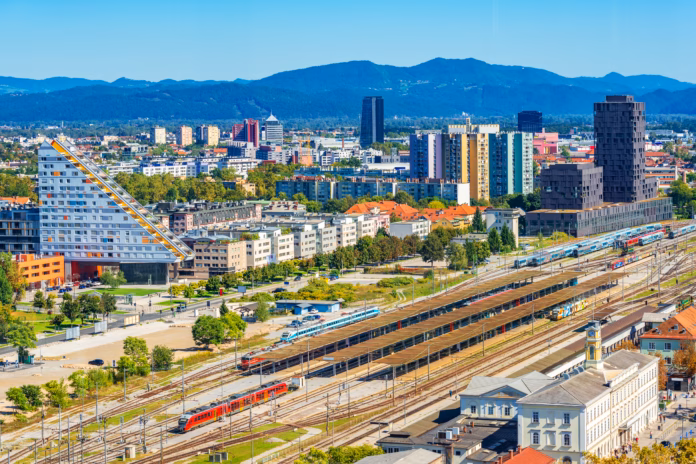 Aerial panorama of Ljubljana with modern buildings, the main train station, trains and beautiful green hills in the background, Slovenia.