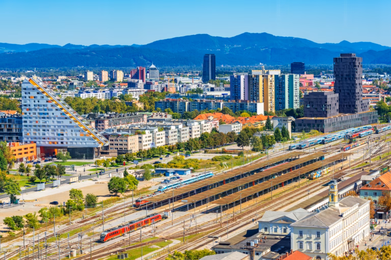 Aerial panorama of Ljubljana with modern buildings, the main train station, trains and beautiful green hills in the background, Slovenia.