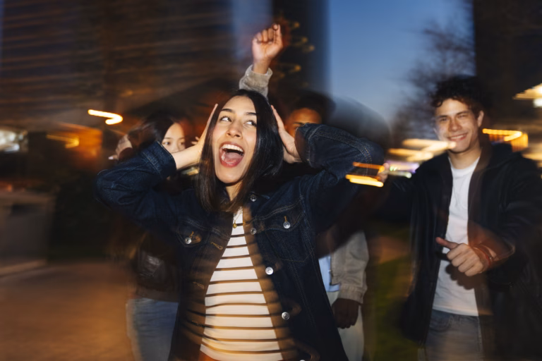 Diverse group of young adult friends dancing and celebrating outdoors at night, motion blur creating dynamic movement
