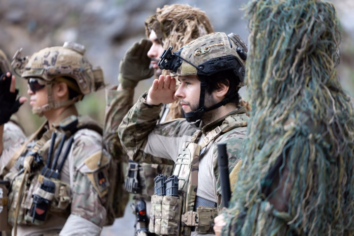 Members of the military unit are lined up in formation. They are saluting while wearing tactical gear