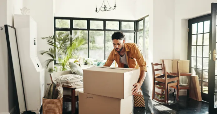 new-house-moving-and-man-with-boxes-real-estate-and-ownership-of-property-with-mortgage-or-lounge-relocation-buyer-and-person-with-cardboard-in-living-room-investment-and-purchase-with-home-loan-stockpack-istock New house, moving and man with boxes, real estate and ownership of property with mortgage or lounge. Relocation, buyer and person with cardboard in living room, investment and purchase with home loan