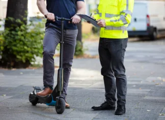 E-skiroji pod drobnogledom: močno se zaostrujejo pravila – to morate vedeti Officer Holding Clipboard In Hand Standing With Man Riding Electric Scooter On City Street
