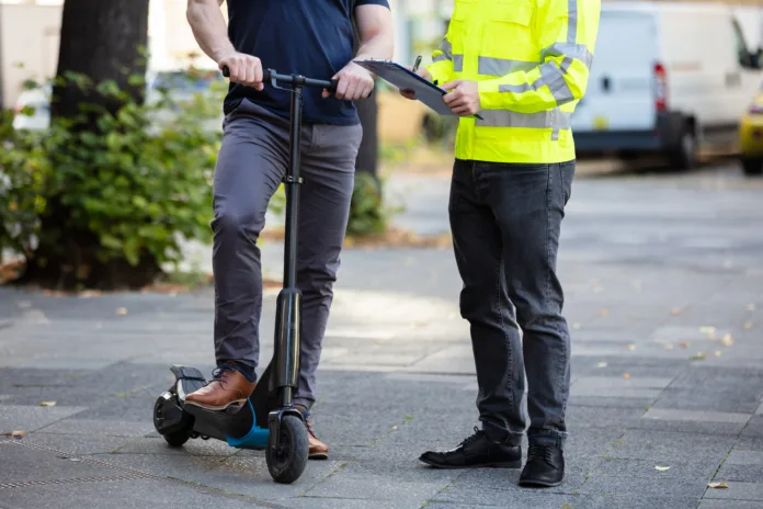 officer-holding-clipboard-in-hand-standing-with-man-riding-electric-scooter-on-city-street-stockpack-istock Officer Holding Clipboard In Hand Standing With Man Riding Electric Scooter On City Street