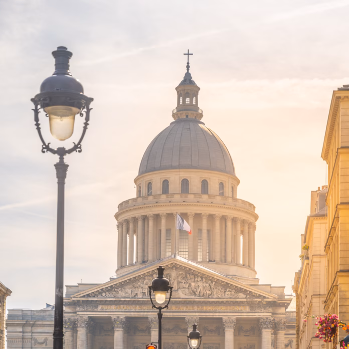 The Pantheon in Paris bathed in the warm glow of a setting sun, with street lamps and a clear sky. Paris, France