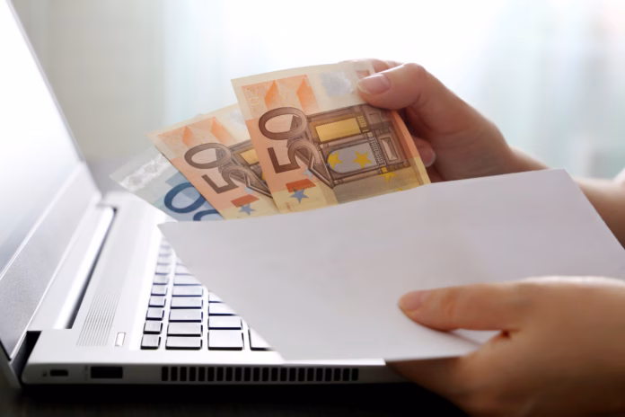 woman-pulls-money-out-of-an-envelope-on-laptop-background-wages-bonus-or-bribe-concept-stockpack-istock Woman pulls money out of an envelope on laptop background, wages, bonus or bribe concept