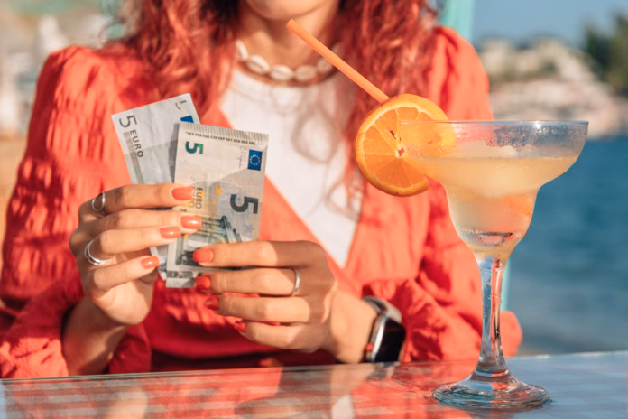 woman-sitting-at-a-beach-cafe-holding-euro-banknotes-and-counting-cash-with-a-smile-cocktail-on-the-table-vacation-setting-stockpack-istock Woman sitting at a beach cafe, holding Euro banknotes and counting cash with a smile, cocktail on the table, vacation setting