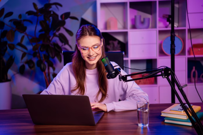 a-young-woman-recording-a-podcast-or-livestream-at-her-desk-in-a-cozy-studio-environment-with-striking-lighting-stockpack-istock A young woman recording a podcast or livestream at her desk in a cozy studio environment with striking lighting.